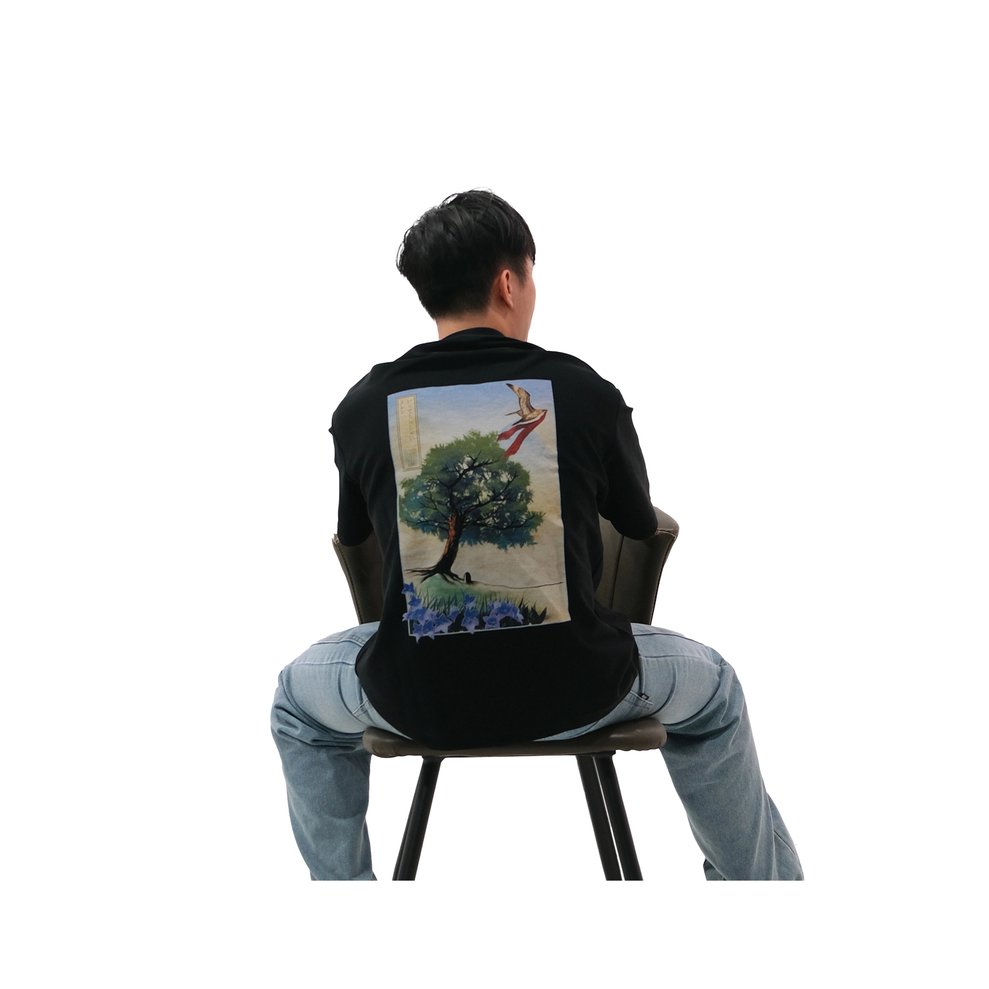 Back view of oversized black NO1 Apparels anime t-shirt, subtle anime streetwear inspired by Attack on Titan See You Later Eren design featuring tree motif, worn by male model sitting on chair.
