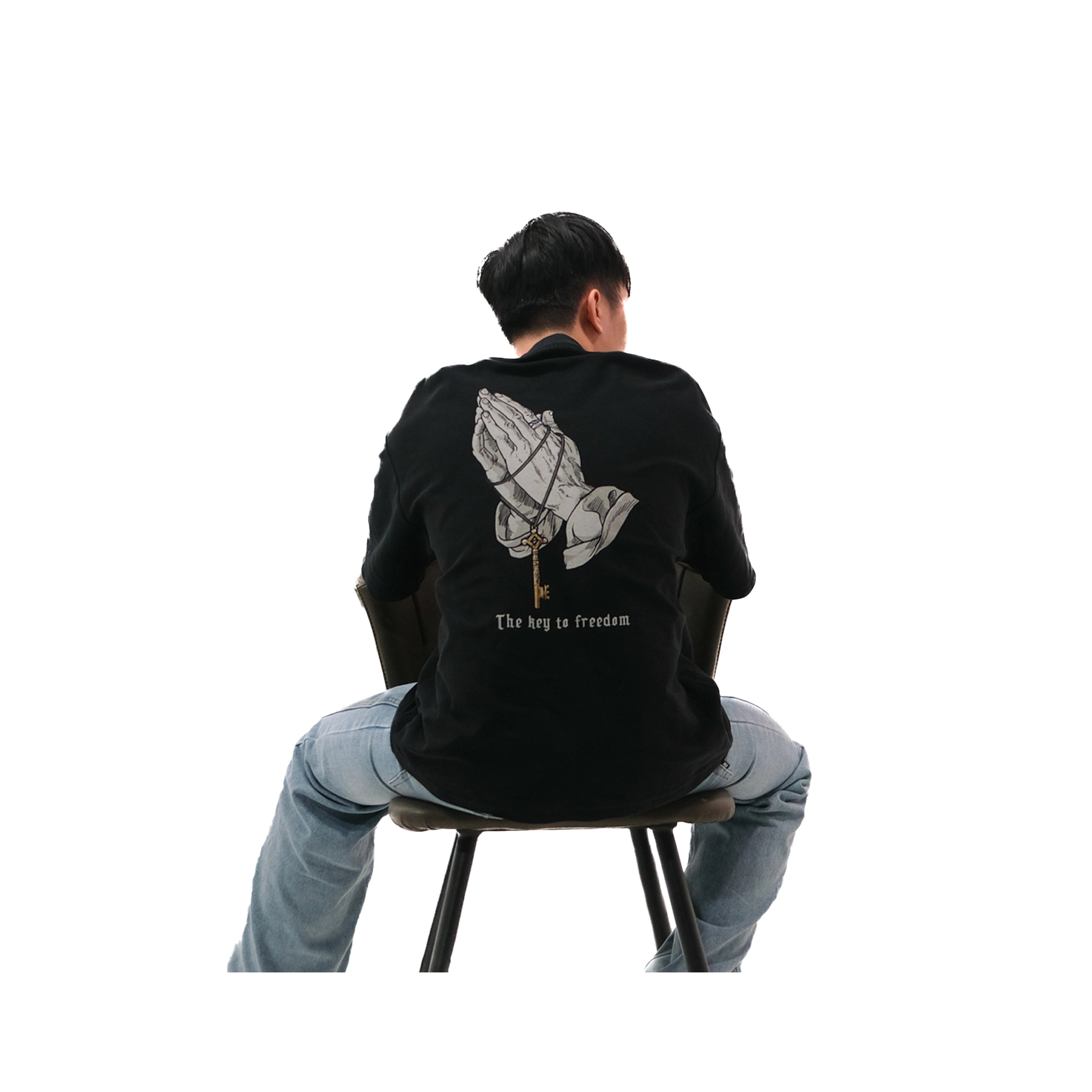 Back view of oversized black NO1 Apparels anime t-shirt, subtle anime clothing inspired by Attack on Titan, Key to Freedom design with basement key motif, worn by male model sitting on chair.