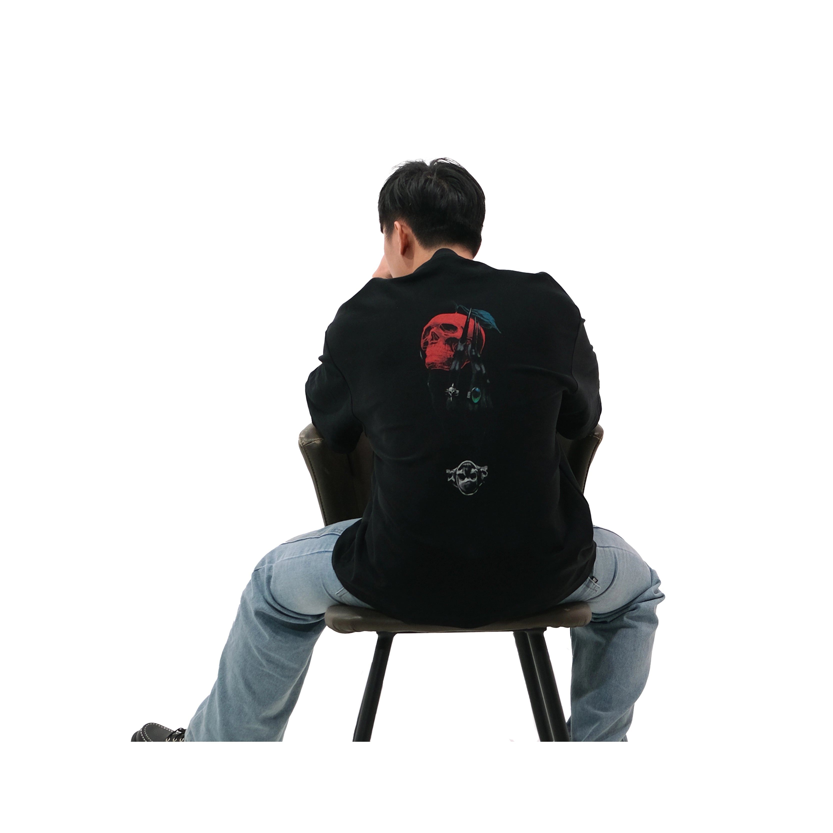 Back view of oversized black NO1 Apparels anime t-shirt, subtle anime streetwear inspired by Death Note Ryuk’s Apple design featuring skull-red apple motif, worn by male model sitting on chair.