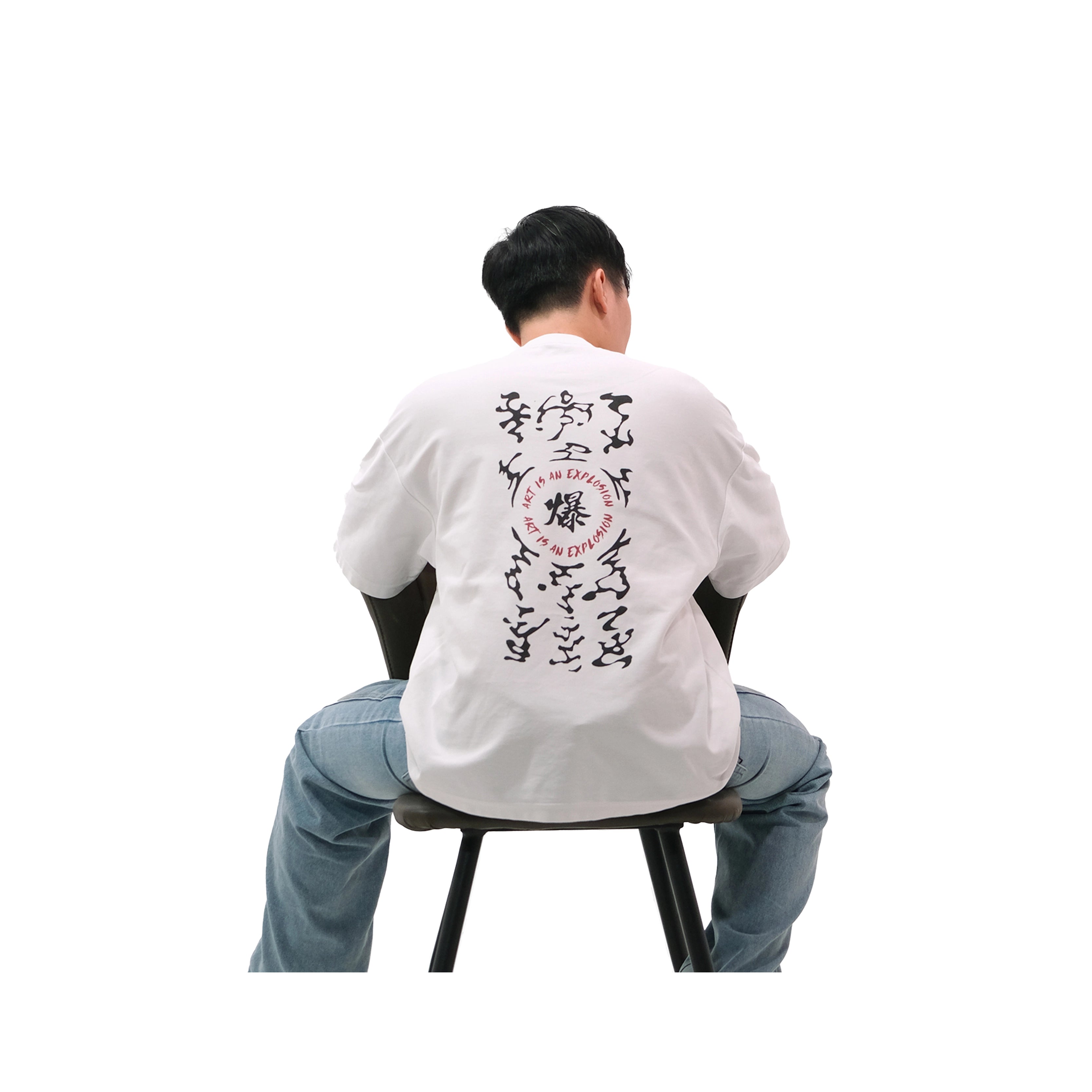 Back view of oversized white NO1 Apparels anime t-shirt, subtle anime streetwear inspired by Naruto Art is an Explosion design with Deidara bomb talisman motif, worn by male model sitting on chair.